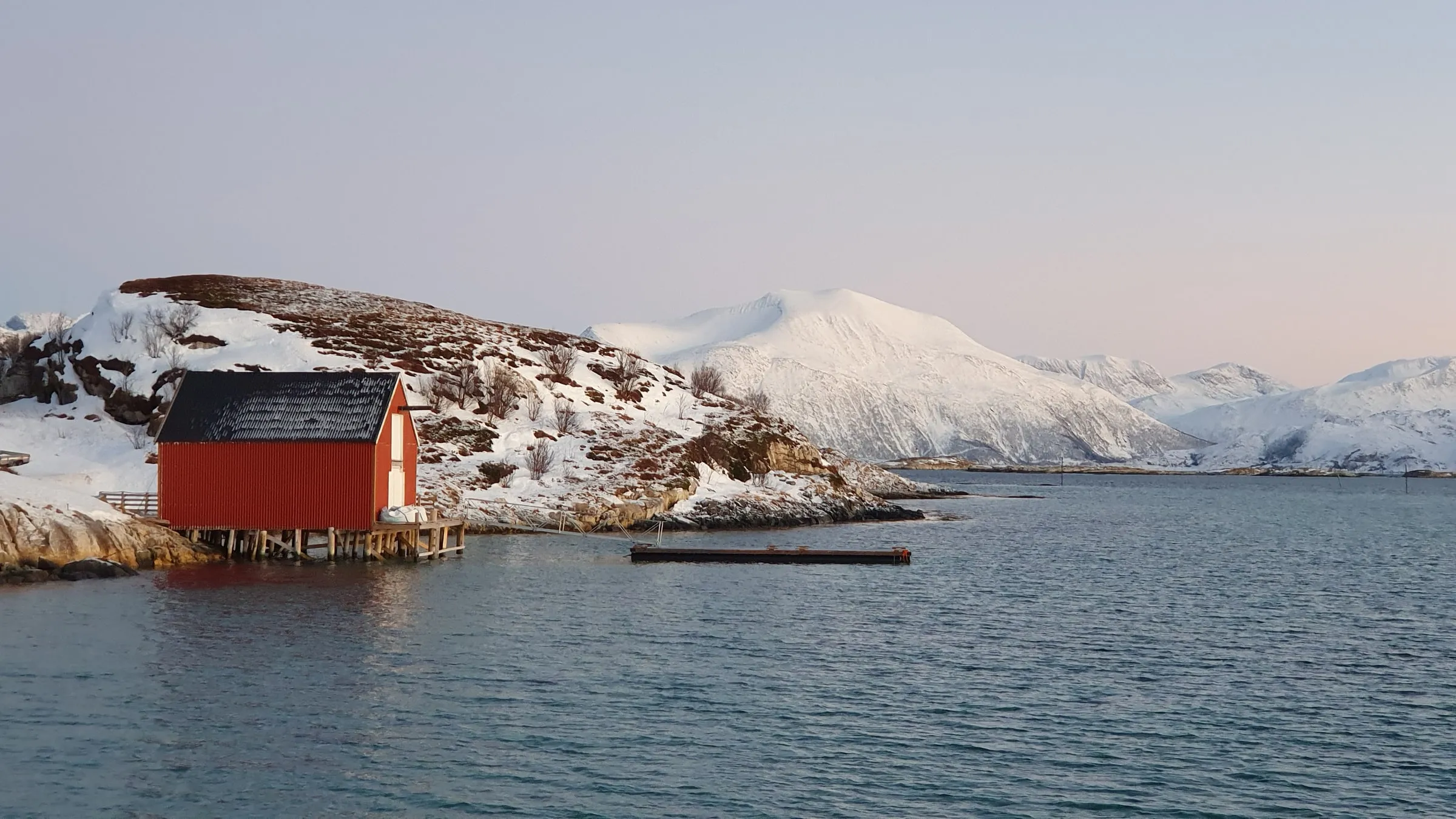 Paesaggio invernale sul mare con una casa rossa e montagne innevate