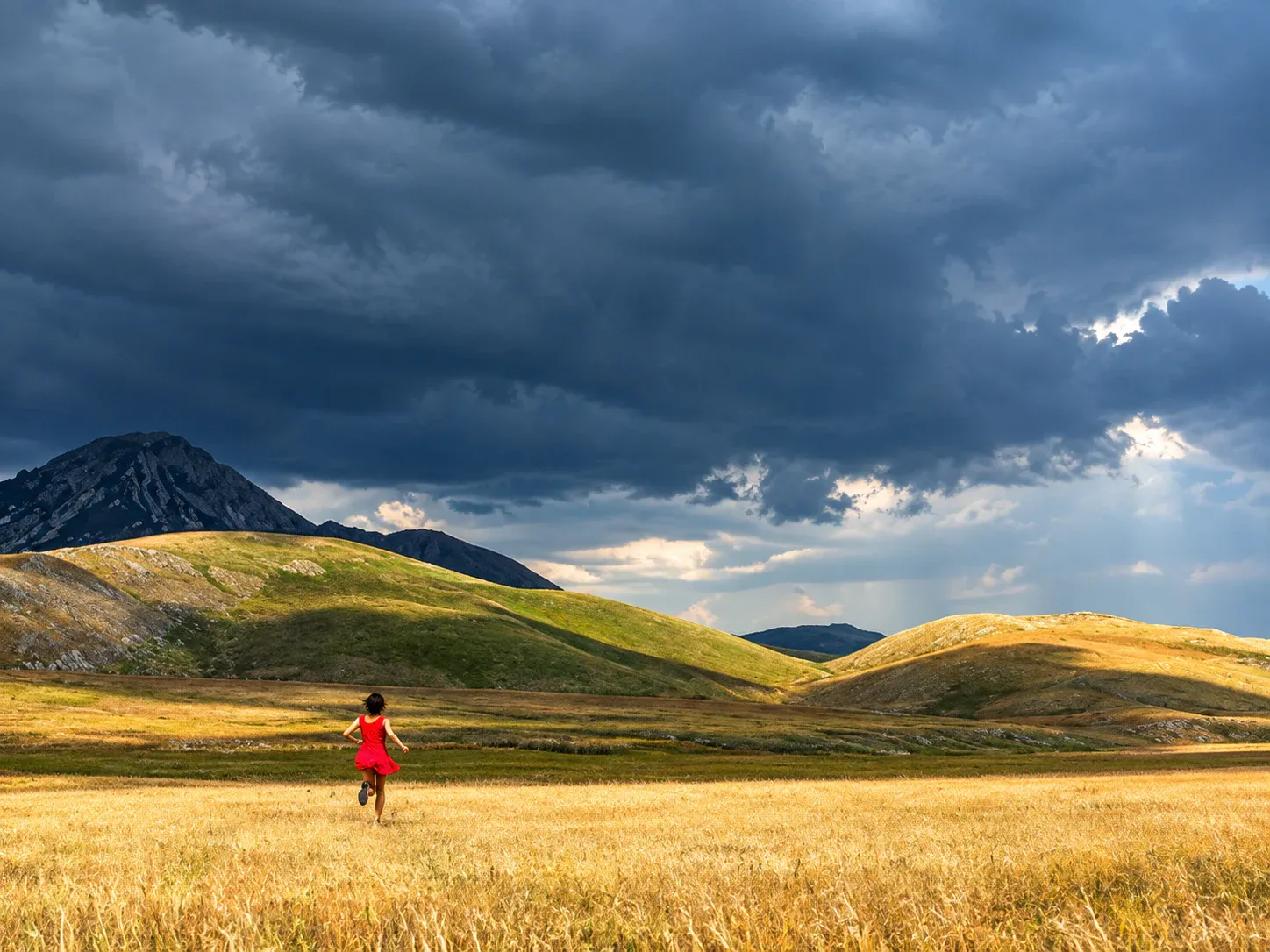 Figura in rosso che corre in un paesaggio montano sotto un cielo temporalesco